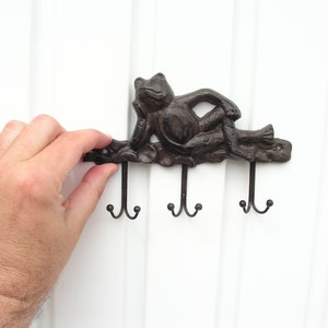 May include: A cast iron frog wall hook with three hooks. The frog is brown and has a relaxed pose. The hooks are black metal.