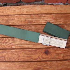 Może przedstawiać: Wzorcowa suwmiarka w zielonym skórzanym etui. Suwmiarka jest wykonana z metalu i ma białą tarczę z czarnymi oznaczeniami. Etui jest zamknięte i ma mały metalowy zatrzask.