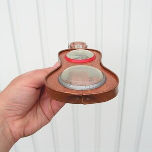 May include: A wooden toy guitar with two round, clear windows. The guitar is brown with a red trim around the windows.