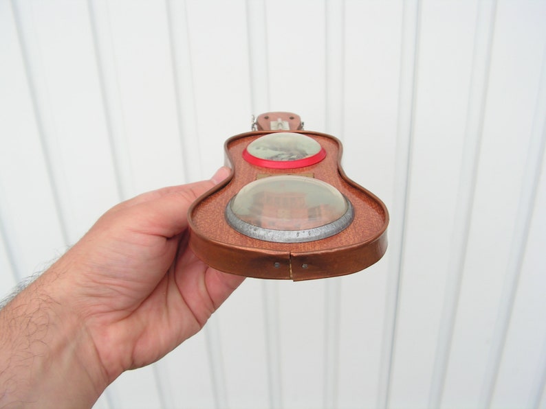 May include: A wooden toy guitar with two round, clear windows. The guitar is brown with a red trim around the windows.