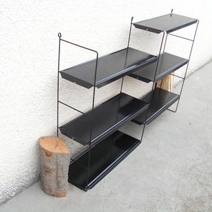 Puede incluir: Una estanter&iacute;a de pared de metal negro con cuatro estantes. Los estantes est&aacute;n inclinados y tienen un acabado negro. La estanter&iacute;a est&aacute; montada en una pared blanca.