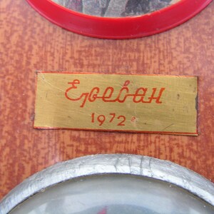 May include: A gold-colored plaque with the text "Ереван 1972" in red lettering. The plaque is mounted on a brown wooden surface.