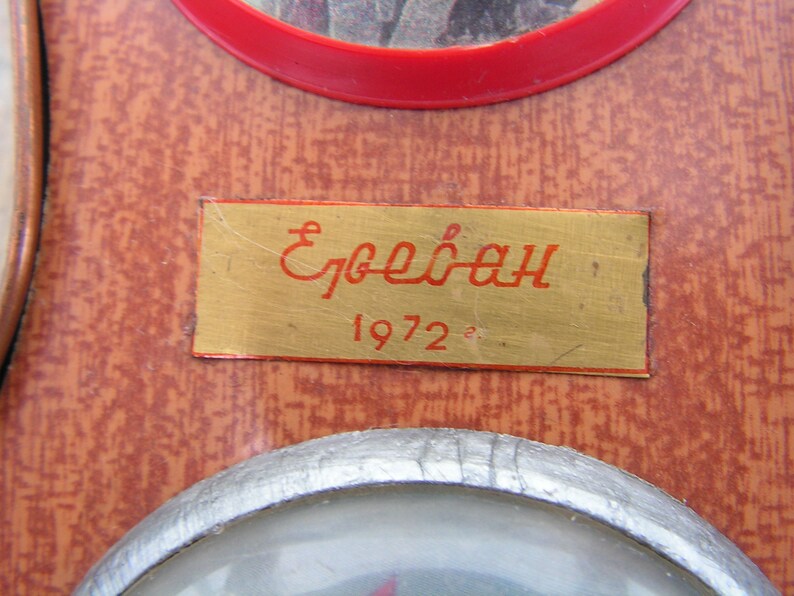May include: A gold-colored plaque with the text "Ереван 1972" in red lettering. The plaque is mounted on a brown wooden surface.