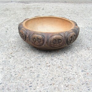 May include: A brown ceramic bowl with a decorative design of faces around the rim.