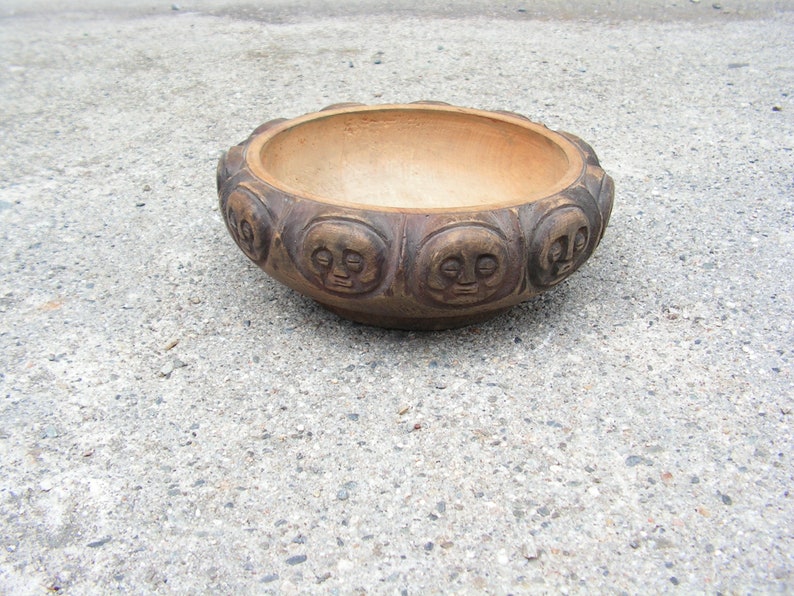 May include: A brown ceramic bowl with a decorative design of faces around the rim.