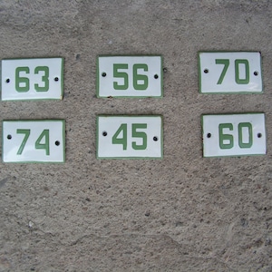 Könnte beinhalten: Sechs weiße Email-Hausnummernschilder mit grünen Zahlen. Die Zahlen sind 63, 56, 70, 74, 45 und 60.