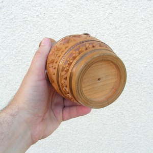 K&ouml;nnte beinhalten: Ein geschnitzter Krug aus Holz mit aufwendigen Details. Der Krug ist braun und hat eine runde Form. Der Boden des Kruges ist sichtbar.