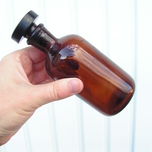 May include: A brown glass bottle with a black plastic lid. The bottle is being held by a hand.
