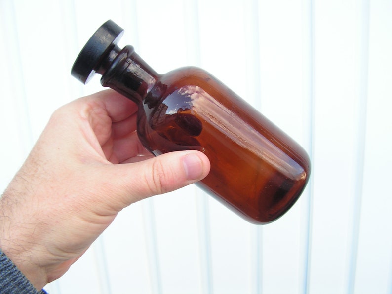 May include: A brown glass bottle with a black plastic lid. The bottle is being held by a hand.