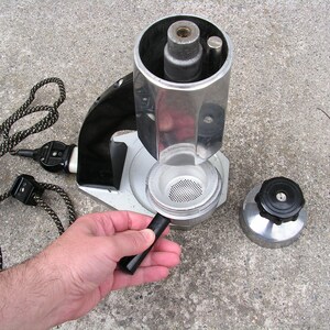 May include: A vintage silver and black electric coffee maker with a removable filter basket and a black handle. The coffee maker is disassembled and the parts are laid out on a gray concrete surface.