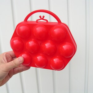 May include: Red plastic egg carrier with a handle. The carrier has 10 individual compartments for holding eggs.