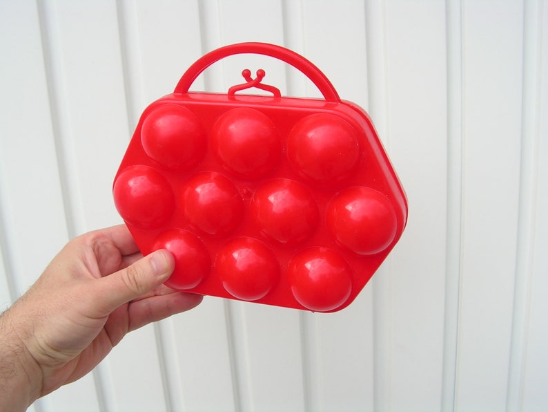 May include: Red plastic egg carrier with a handle. The carrier has 10 individual compartments for holding eggs.