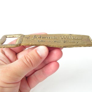 May include: A gold-coloured metal bottle opener with the words "Johnnie Walker Old Scotch Whisky" embossed on the front.