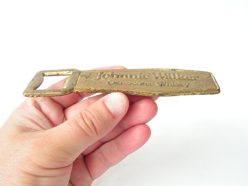 May include: A gold-coloured metal bottle opener with the words "Johnnie Walker Old Scotch Whisky" embossed on the front.