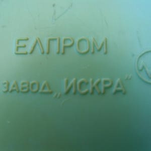May include: A close-up of a green plastic object with the text "EЛПРOМ ЗАВОД, ИСКРА" and a symbol of a lightning bolt in a circle.