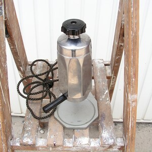May include: A silver and black electric coffee maker with a cord and a black handle. The coffee maker is sitting on a wooden step stool.