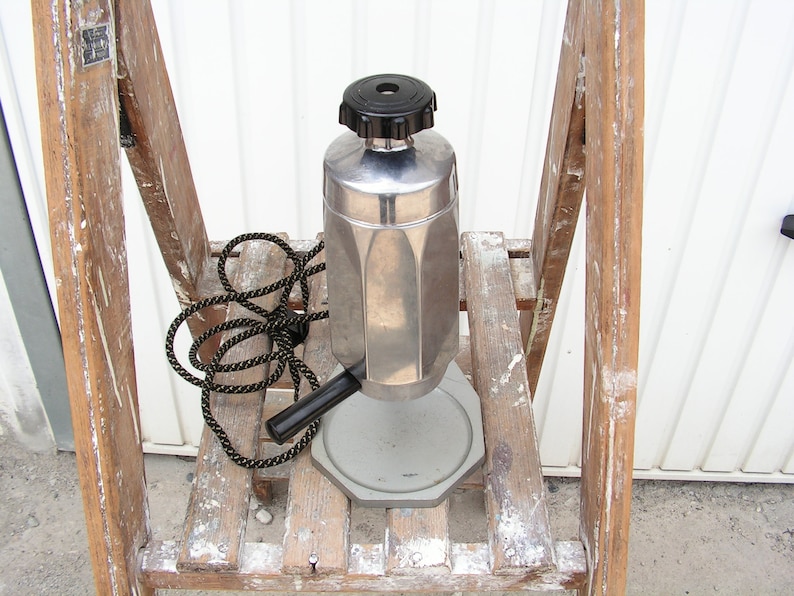 May include: A silver and black electric coffee maker with a cord and a black handle. The coffee maker is sitting on a wooden step stool.