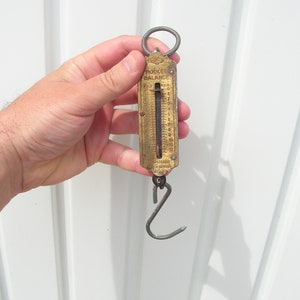 May include: A vintage brass pocket balance scale with a hook on the bottom and a graduated scale on the front. The scale reads "Pocket Balance" and "Sterling Silver".