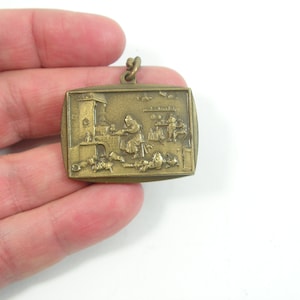 May include: A gold-toned metal keychain featuring a raised relief image of a scene with people and a building. The scene is reminiscent of a historical painting.