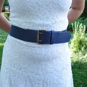 May include: A white lace dress with a blue elastic belt. The belt has a gold buckle.