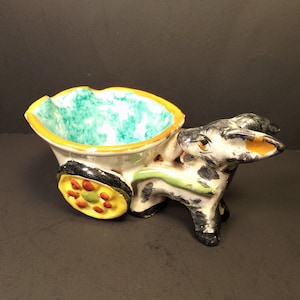 May include: A ceramic donkey pulling a small cart with a turquoise and white interior. The donkey is painted black, white, and yellow. The cart has a yellow wheel with red and green accents.