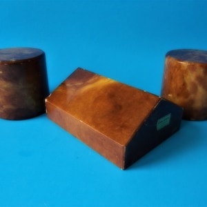 Pode incluir: Conjunto de três prendedores de livros de mármore castanho e amarelo. Dois são cilíndricos e um tem a forma de uma casa.