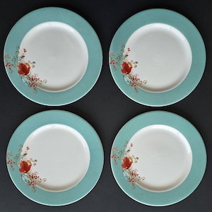May include: A set of four round ceramic plates, each featuring a solid white center and a wide, solid teal border. A delicate floral pattern in shades of red, orange, and light blue is printed on the left side of each plate, extending slightly from the border.