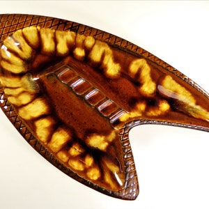 May include: A brown and yellow ceramic ashtray shaped like a fish with a geometric pattern around the edge.