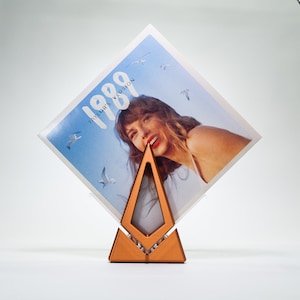 May include: A copper-colored triangular record stand with a record on top. The record cover features a woman with blonde hair and the text "1989 Taylor's Version".