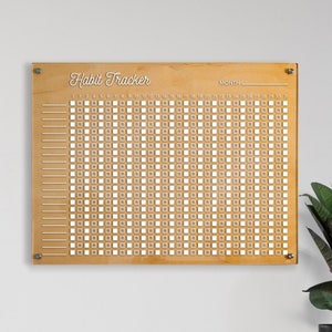 May include: A wooden habit tracker with a white grid and the text "Habit Tracker" and "MONTH" printed on it.