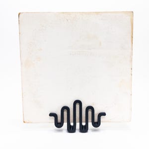 May include: A black metal photo stand with a wavy design. The stand is holding a blank white card.