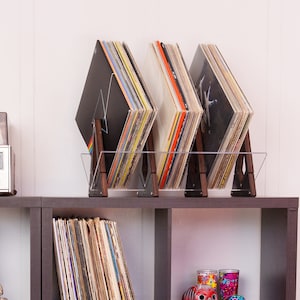 May include: A clear acrylic record stand with three vinyl record albums. The stand has a black metal frame and is holding three vinyl records. The records are all different colours and have different album covers.