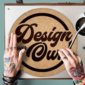 Könnte beinhalten: Eine Korkplatte mit dem Text "Design Your Own" in schwarzen Buchstaben auf braunem Hintergrund. Die Platte befindet sich auf einem Plattenspieler.