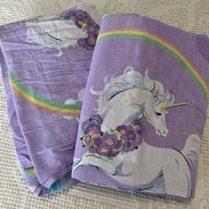 May include: Purple and white twin-sized bed sheets featuring a unicorn and rainbow design.