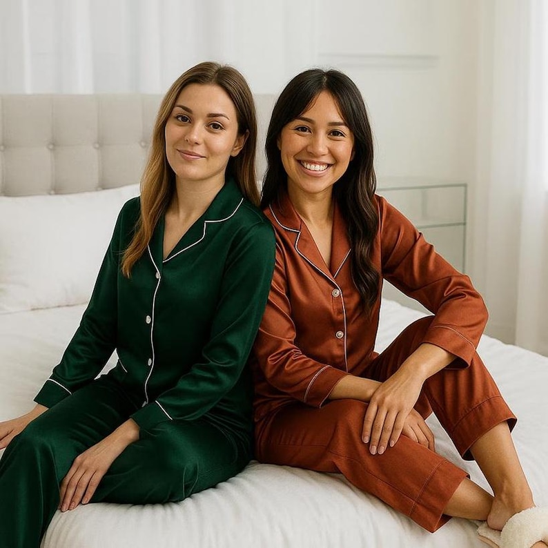 May include: Two people wearing matching satin pajamas. One set is dark green, the other is rust-colored. Both sets have white piping and button-up tops. The pajamas are a classic, comfortable sleepwear style.