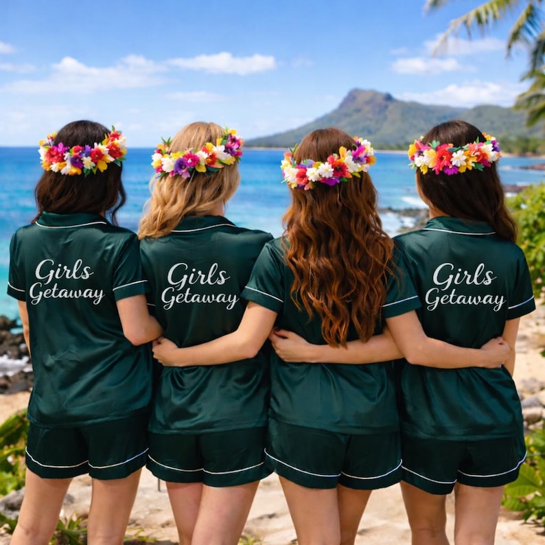 May include: Four people wearing matching dark green pajama sets with white trim and floral headbands stand on a beach. The text "Girls Getaway" is printed on the back of each shirt. The ocean and a mountain are visible in the background.