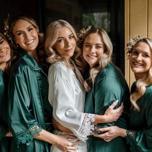 May include: Four individuals wearing emerald green satin robes with lace-trimmed sleeves and one individual wearing a white satin robe with lace-trimmed sleeves. Each robe features a notched collar and a smooth, shiny finish with delicate floral hair accessories.