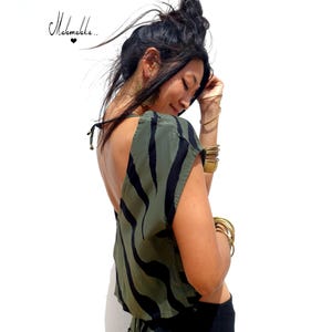 Puede incluir: Top verde oliva con estampado de rayas de cebra negras y espalda baja. La modelo lleva pulseras y pendientes dorados. La parte superior está atada a los hombros. El top es sin mangas.