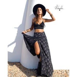 Puede incluir: Una mujer con un top negro, una falda larga negra con un patrón geométrico y un sombrero negro. La falda tiene una abertura alta. La imagen incluye el texto "Mahamala..." en cursiva.