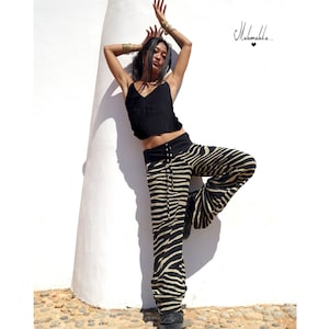 Puede incluir: Una mujer con un top negro de tirantes y pantalones de estampado de cebra posa contra una pared blanca. Los pantalones tienen una cintura negra y un cordón.