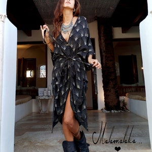 May include: A black and white patterned dress with a V-neck and a tie at the waist. The dress is paired with black boots. The image also includes a silver necklace and bracelets. The word "Malamalaka" is written in cursive.