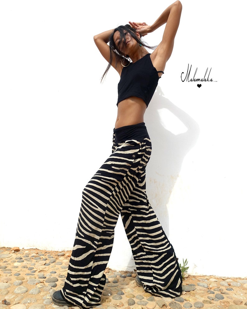 May include: A woman wearing a black crop top and wide-legged trousers with a zebra print. The trousers have a black elastic waistband and a black drawstring. The woman is standing in front of a white wall with the text "Malamakka..." written on it.