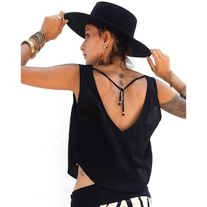 Puede incluir: Una camiseta sin mangas negra con cuello en V profundo y espalda baja. La camiseta se combina con un sombrero negro y pulseras doradas. La modelo lleva una parte inferior con estampado en blanco y negro.