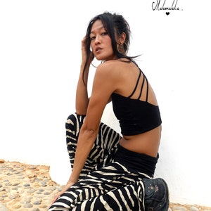 May include: A woman wearing a black crop top and zebra print trousers sits on a bed of small stones. The text "Makamaka..." is written in black on a white background above her head.