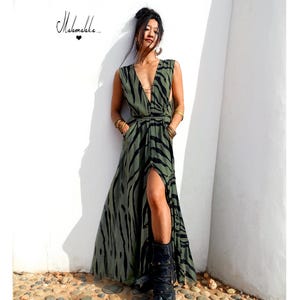 May include: An olive green maxi dress with a black zebra stripe pattern. The dress has a V-neck, a high slit, and a tie at the waist. The dress is sleeveless and has pockets. The text "Mahamala.." is in the upper left corner.