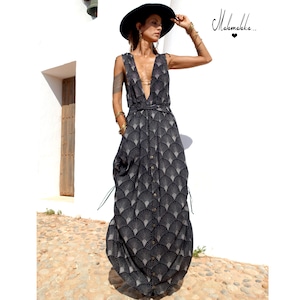 May include: A sleeveless, floor-length dress with a black and white fan-shaped pattern. The dress features a deep V-neck, a button-down front, and a matching belt. The model is wearing a black hat and gold jewelry.