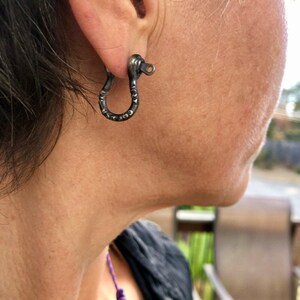 May include: A pair of silver hoop earrings with a textured, hammered finish. The earrings are in the shape of a small, open circle.