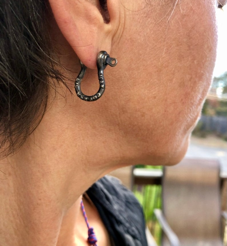 May include: A pair of silver hoop earrings with a textured, hammered finish. The earrings are in the shape of a small, open circle.