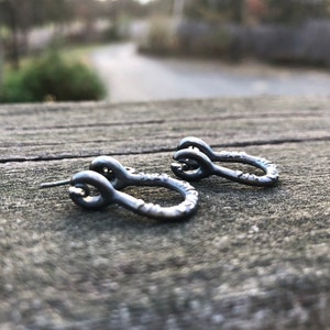 May include: A pair of small, silver hoop earrings with a textured finish. The earrings are in the shape of a circle with a small loop at the top.