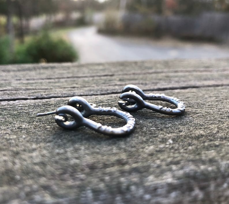May include: A pair of small, silver hoop earrings with a textured finish. The earrings are in the shape of a circle with a small loop at the top.